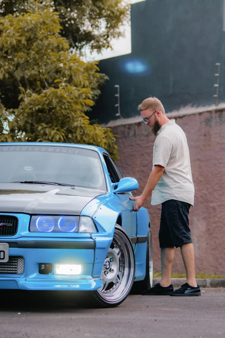 Yuri beside his blue BMW E36, holding the door handle.